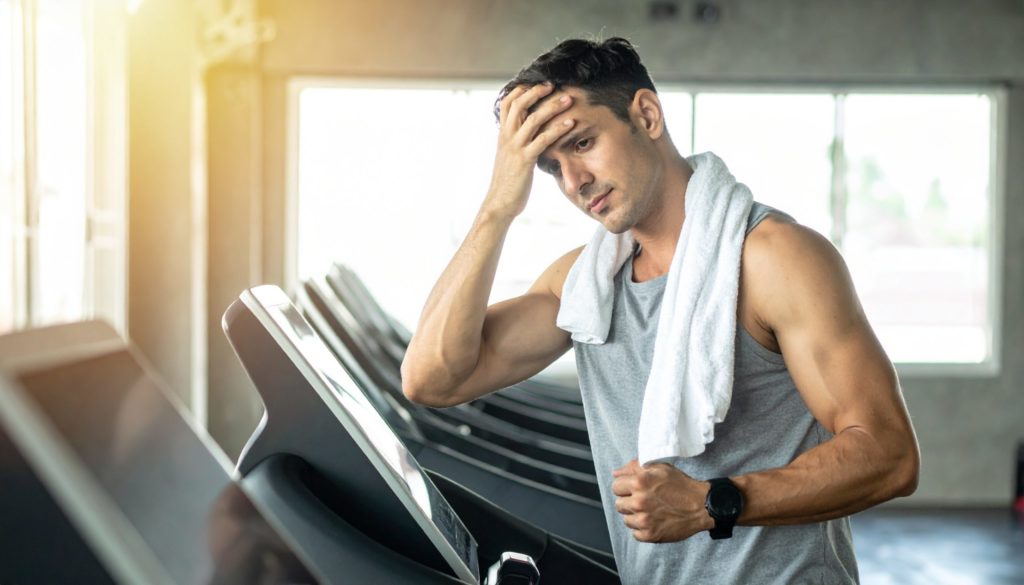 ランニングマシーンの上で少し気分が悪そうに頭を押さえている人