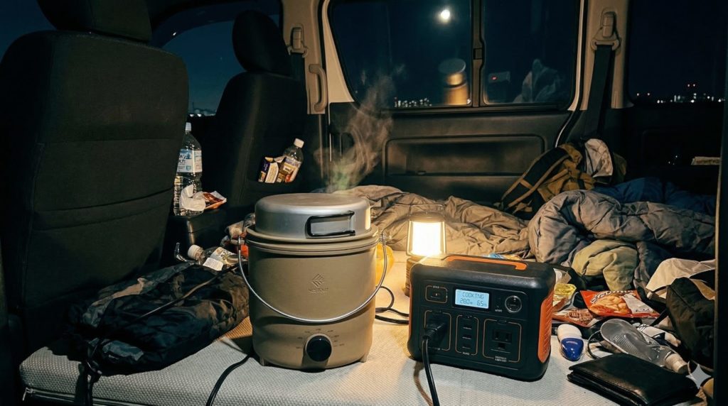 薄暗いリアルな車中泊の車内で、ポタ電に繋がれたCOOKER-1が湯気を立てている写真。